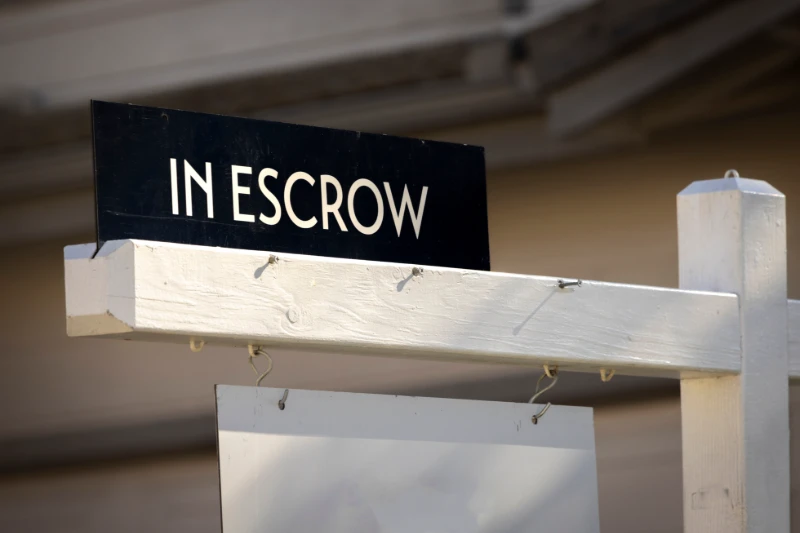 A residential real estate sale sign in English with the words In Escrow written in white letters